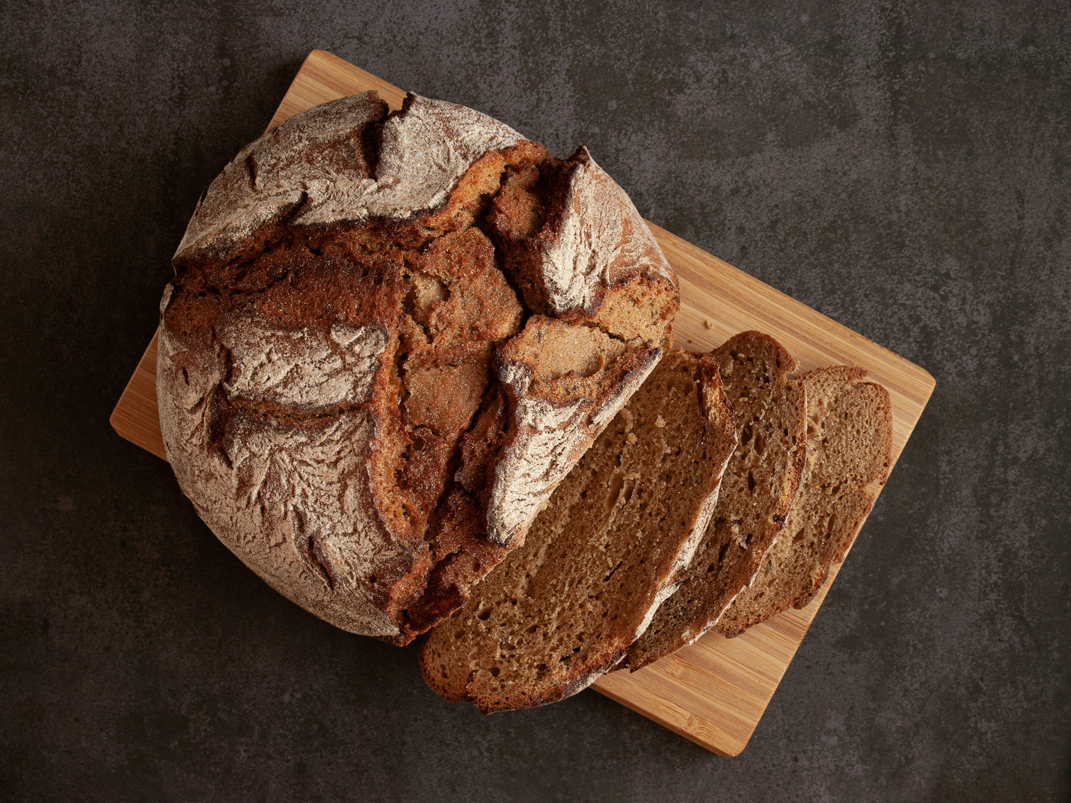 Loaf of bread with slices on a wooden board against a dark background