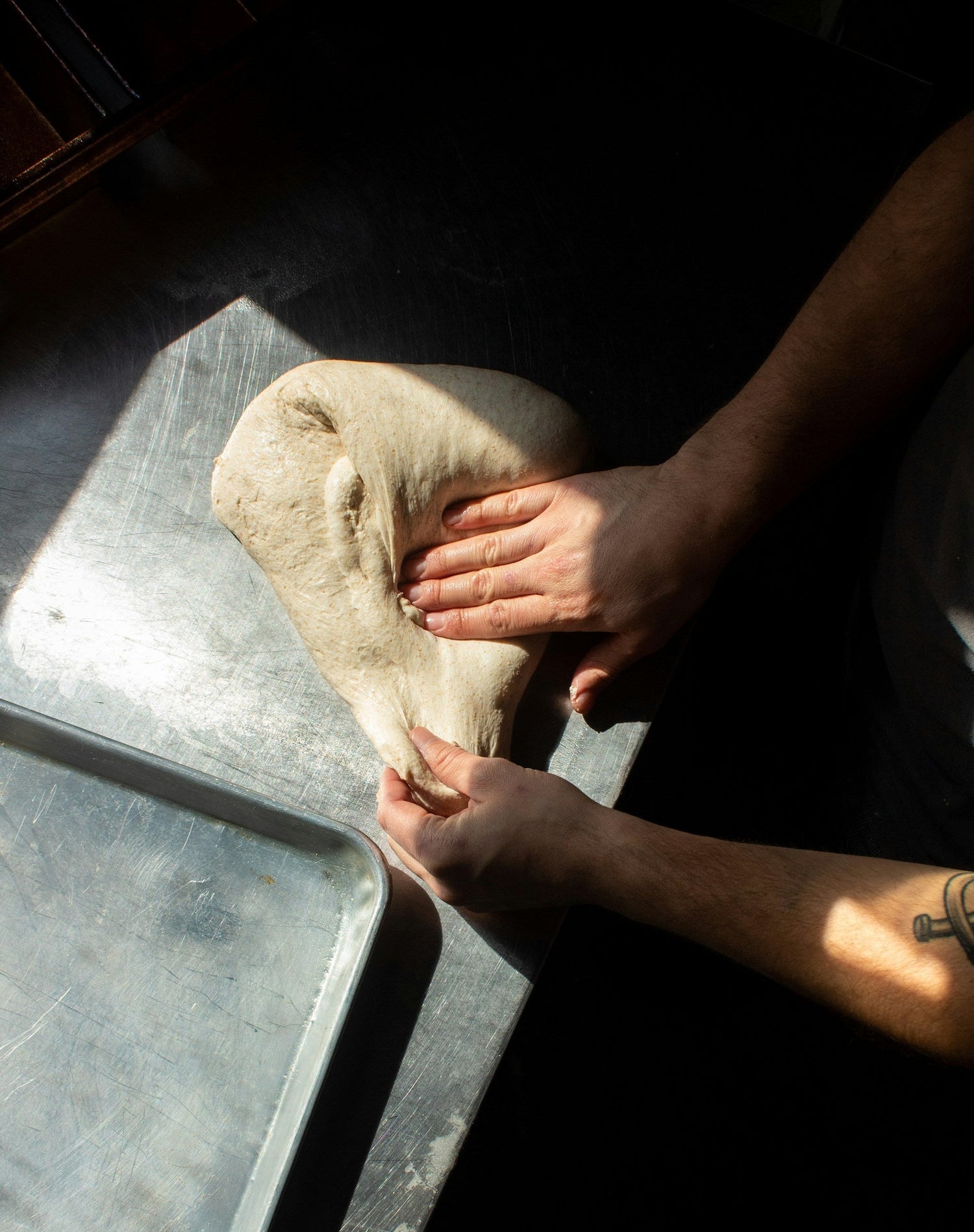 Person holding a piece of dough on a metal surface